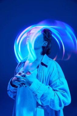 Neon ışıklar ve canlı renkler arasında poz veren kıvırcık saçlı çekici genç adamın yaratıcı portresi hareket bulanıklığı içindeki canlı geometrik figürleri aydınlattı. Güzellik kavramı, kendini ifade etme, duygular.