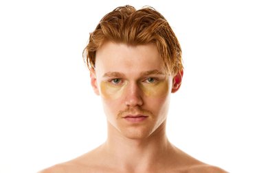 Gözlerinin altında hidrojel bantlarla beyaz stüdyo arka planına bakan genç adamın portresini yakından çek. Doğal güzellik kavramı, bencillik, vücut ve cilt bakımı, moda, kozmetoloji ürünü.