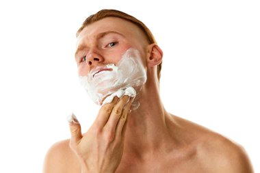 Hijyen tedavileri. Tıraş köpüğü kullanan çekici bir adam beyaz stüdyo arka planında kameraya bakıyor. Doğal güzellik kavramı, kişisel bakım, vücut ve cilt bakımı, berber, yüz bakımı, tarz. Ad