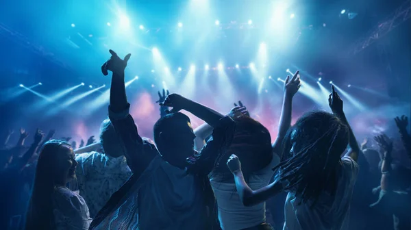 Happy, overjoyed people, students dancing raising hand and singing in neon light, spotlights indoor on party. Concept of party, festivals, concerts, music and dance, holidays, lifestyle, event.