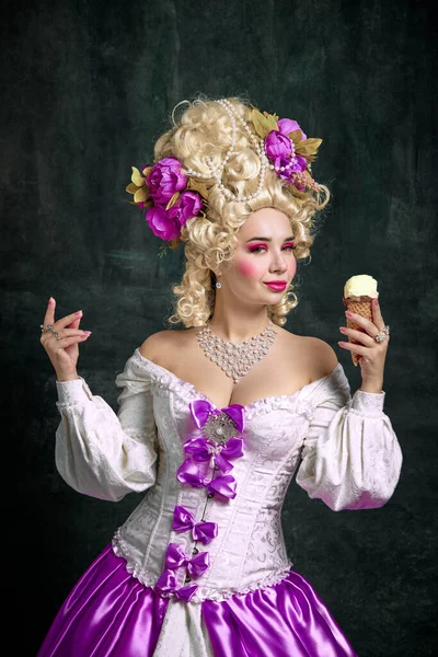 Portrait of aristocratic medieval person, woman looking playful to camera and holding cold tasty ice cream against vintage background. Concept of food, nutrition, catering, restaurant menu, delivery.