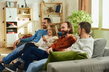 Grup fotoğrafı. Erkekler ve kızlar oturma odasında kanepede oturup tüm zamanlarını komedi dizileri izleyerek geçiriyorlar. Arkadaşlık kavramı, birliktelik, çevrimiçi etkinlik, eğlence, olumlu duygular..
