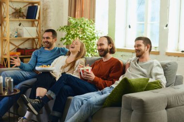 Grup fotoğrafı. Erkekler ve kızlar oturma odasında kanepede oturup tüm zamanlarını komedi dizileri, TV dizileri izleyerek geçiriyorlar. Arkadaşlık kavramı, birliktelik, TV programı, online etkinlik, eğlence.