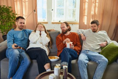 Grup fotoğrafı. Cadılar Bayramı akşamı evde oturma odasındaki kanepede oturan kızlar ve erkekler korku filmi izliyorlar. Arkadaşlık kavramı, birliktelik, TV programı, online etkinlik, eğlence.