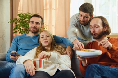 Bir grup mutlu, komik insan en sevdikleri TV dizisini izlerken abur cubur yiyor, futbol maçı oturma odasında koçun başında oturuyor. Arkadaşlık kavramı, birliktelik, TV programı, online etkinlik, eğlence.