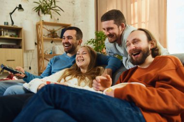 Şok olmuş genç ve çekici insanlar, geniş bir gülümsemeyle, oturma odasındaki kanepede oturmuş komik entrikalı bir film seyrederek gülüyorlar. Arkadaşlık kavramı, birliktelik, TV programı, online etkinlik, eğlence.