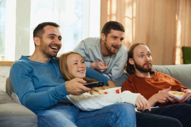 Gencecik, çekici insanları gülümseyerek şoke etti. Oturma odasındaki kanepede oturmuş komedi komedisiyle film izlerken kahkahalar attı. Arkadaşlık kavramı, birliktelik, TV programı, online etkinlik, eğlence.
