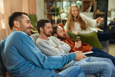 Oturma odasındaki kanepede oturup komedi dizisi, televizyon dizisi izlerken tartışan mutlu insanların yan görüntüsü. Arkadaşlık kavramı, birliktelik, TV programı, online etkinlik, eğlence