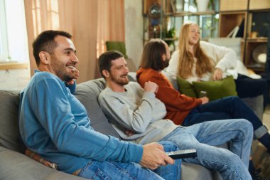 Oturma odasındaki koltukta oturup komedi filmi, televizyon programı izlerken tartışan mutlu insanların yan görüntüsü. Seçici odaklanma. Arkadaşlık kavramı, birliktelik, TV programı, online etkinlik.