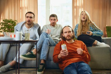 Oturma odasındaki kanepede oturup futbol maçı izleyen neşeli arkadaş grubunun alt görüntüsü. Futbol şampiyonası. Arkadaşlık kavramı, birliktelik, TV programı, online etkinlik, eğlence.