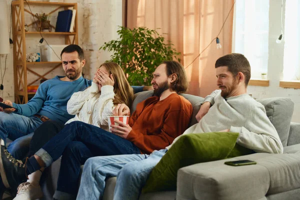 Grup fotoğrafı. Kızlar ve erkekler korku filmi izliyor, Cadılar Bayramı akşamı evde oturma odasında kanepede oturuyorlar. Arkadaşlık kavramı, birliktelik, TV programı, online etkinlik, eğlence.