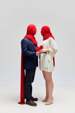 Abartılı duygular. Tanımlanamayan çift, kumaş kafalı kadın ve erkek, beyaz stüdyo geçmişine karşı kırmızı kağıt kalp taşıyor. Garip aşk kavramı, modern ilişki, Sevgililer Günü