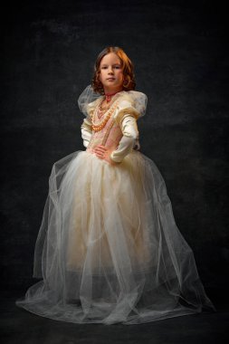 Kraliyet mensubu gibi giyinmiş, eski moda elbiseli ve klasik arka planda duran küçük bir kızın tam boy portresi. Tarihi yeniden yapılanma kavramı, çağların karşılaştırması, moda.