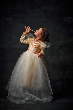 Küçük ortaçağ insanının tam boy portresi, eski moda kostüm giymiş küçük bir kız eski moda arka planda tatlı şekerlemeler yiyor. Ortaçağ modasının mukayese kavramı.