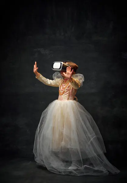 Full-length portrait of medieval person, old-fashioned girl playing games in VR glasses against dark vintage background. Concept of historical remake, comparison of eras, medieval fashion, emotions.