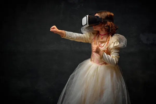 Portrait of aristocratic medieval person, little princess playing games in modern VR glasses against dark vintage background. Concept of historical, comparison of eras, medieval fashion, emotions.