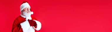 Pankart. Şok olmuş, gri sakallı, Noel Baba kostümlü olgun bir adamın portresi. Kırmızı arka planda, mesaj için negatif alan var. Kış tatili kavramı, Mutlu Noeller, neşe, eğlence