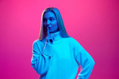 Çekici bir kadın parmağını dudaklarının üzerinde tutuyor, mavi neon ışıkta pembe arka planda sessizlik işareti gösteriyor. İnsan duyguları kavramı, yüz ifadesi, alışveriş satışları, kış tatilleri.