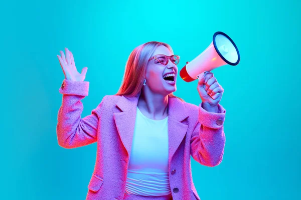 Portrait of young woman loudly screaming to loudspeaker about starting sales season against gradient background illuminated mixed colors neon light. Concept of shopping, fashion, communication.