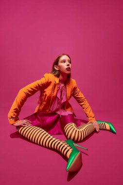 Dışavurumcu genç kızın tam boy portresi, alışılmadık, turuncu çizgili tayt, uzun etek ve mor arka planda kısa ceket giyen bayan. Sürrealizm, sanat, retro moda kavramı.