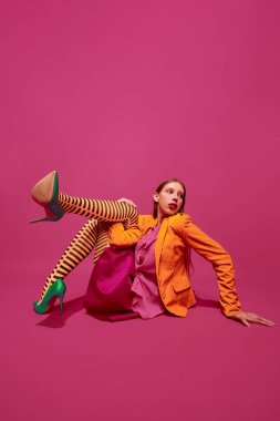 Olağanüstü bir moda kıyafeti. Renkli, şık çizgili turuncu tayt giymiş, eteği morumsu arka planda poz veren genç bir kız. Sürrealizm kavramı, sanat, yüksek, güzellik, reklam.