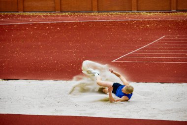 Etkileyici bir atlayıştan sonra kum havuzu inişi. Motive olmuş genç bir adamın portresi, profesyonel sporcu şampiyonluk için mükemmel uzun atlama yapıyor. Spor, motivasyon, enerji kavramı.