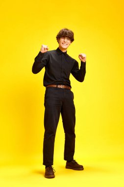 Mutlu, neşeli genç bir adamın uzun boylu portresi, iş hayatında başarı göstergesi olarak ellerini sıktı ve sarı stüdyo arka planına karşı çalıştı. İnsan duyguları kavramı, doğru yol. Ad