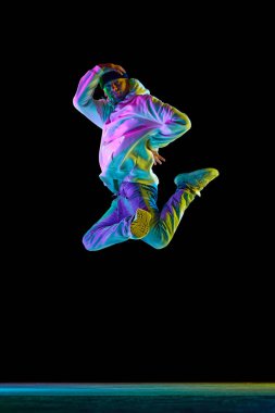 Stüdyoda, esnek, spor yapan, break dans yapan, zıplayan, neon ışıkta siyah arka planda donan genç bir adamın görüntüleri. Gençlik kültürü kavramı, aktif yaşam tarzı, yaratıcılık, sanat.
