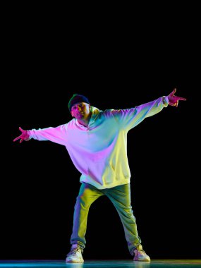 Hey-yo. Modern dans. Hip-hop erkek dansçı, atletik adam neon ışıkta siyah arka planda şık bir şekilde dans ediyor. Gençlik kültürü kavramı, aktif yaşam tarzı, tarz ve moda, yaratıcılık, sanat
