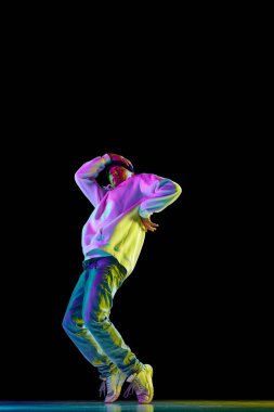 Genç, şık bir adam, break dans dansçısı. Dans salonunda siyah arka planda günlük kıyafetlerle dans ediyor. Gençlik kültürü kavramı, aktif yaşam tarzı, tarz ve moda, sanat.