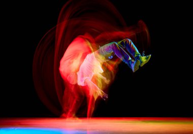 Hip-hop erkek dansçı, atletik adam siyah arka planda hareket bulanıklığıyla karışık neon ışıkta şık bir şekilde dans ediyor. Gençlik kültürü kavramı, aktif yaşam tarzı, tarz ve moda, yaratıcılık.