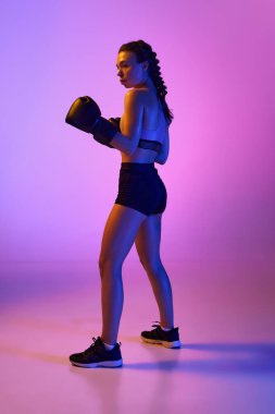 Güçlü bayan boksörün spor portresi, profesyonel MMA sporcusu neon ışıkta pembe menekşe stüdyosuna karşı. Spor anlayışı, aktif yaşam tarzı, sağlık, rekabet.