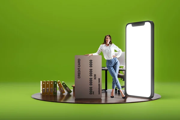 Smiling young woman standing with big credit card near giant 3D model of mobile phone with empty screen over green background. Online shopping, sales. E-commerce. Mockup for text, ad, design, logo