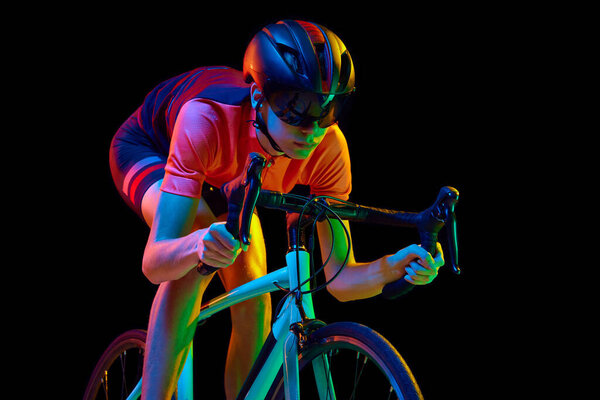 Сконцентрированный молодой человек, спортсмен в спортивной одежде, очках и шлемах, катающийся на велосипеде, изолированном на черном студийном фоне в неоновом свете. Мбаппе спорта, действия, конкуренции, силы, выносливости