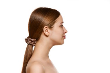 Profil portresi, çıplak omuzlu, tertemiz ciltli, izole beyaz arka planlı güzel bir genç kadın. Kavramsal gençlik, doğal güzellik, sağlıklı yaşam tarzı, cilt bakımı kozmetik. Ad