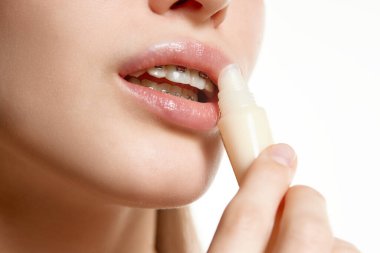 Beyaz arka planda genç bir kadın modelin kopyalanmış portresi. Kadın dudaklarına doğal merhem sürmüş. Dolgun dudakların ve kadın teninin doğal parlaklığı. Gençlik kavramı, doğal güzellik, cilt bakımı, makyaj.