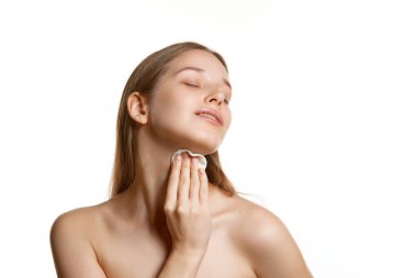 Cildi iyi korunmuş kadın portresi beyaz arka planda pürüzsüz cilt için vitaminli ve mineralli süngerle deriyi siler. Kavramsal gençlik, doğal güzellik, cilt ve vücut bakımı. Ad