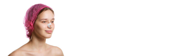 Баннер. Портрет привлекательной женщины в розовой кепке с гипсами на носу после ринопластики на белом студийном фоне с копировальным пространством. Концепция медицины, инъекции красоты, пластическая хирургия тела.