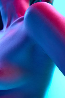 Çıplak kadın vücudunun yakın plan görüntüsü, göğüs ve omuz, neon ışıkta mavi arka plan. Vücut estetiği, sanat, güzellik, şehvet, çıplaklık, sağlık hizmetleri, kadınlık kavramı