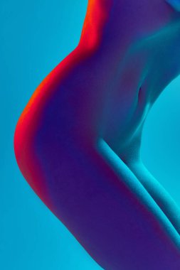 Seksi, çıplak bir kadın vücudu, ince bir göbek, parlak ışıkta kalçaları mavi arka planda. Seksi vücut şekli. Vücut estetiği, sanat, güzellik, şehvet, çıplaklık kavramı.