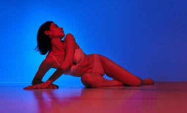 Modern cazibeyle ışıldıyor. Neon ışıklı parlak ışıkta arka planda poz veren genç bir kadının tam boy portresi. Sanat anlayışı, kadın sağlığı, sağlık, kendini ifade etme.