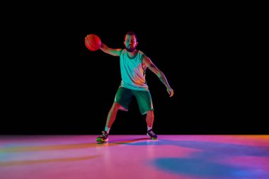 Profesyonel basketbolcunun dinamik portresi, keskin top sürme ve neon arka planda güçlü smaç basma becerileri. Spor anlayışı, hobi, aktif yaşam tarzı.