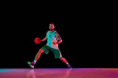 Dinamik çekim, yetenekli basketbolcuyu iş başında yakalıyor. Neon ışıkta siyah arka plana karşı yoğun antrenman sırasında odaklanmış ve kararlı. Spor anlayışı, hobi, aktif yaşam tarzı.