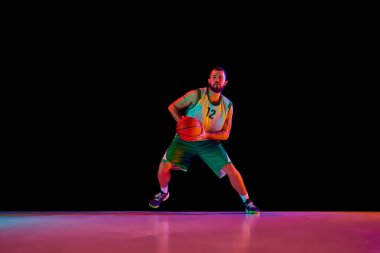 Sporcunun tam boy portresi, profesyonel basketbolcu neon ışıkta siyah arkaplanla karşılaşmadan önce aktif olarak antrenman yapıyor. Spor anlayışı, hobi, aktif yaşam tarzı. Boşluğu kopyala, ad