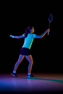 Genç bir kızın dikiz aynasındaki portresi, yetenekli badminton oyuncusu neon ışıkta siyah arka plana karşı yoğun bir şekilde çalışıyor. Spor anlayışı, aktif yaşam tarzı, eylem. Boşluğu kopyala.