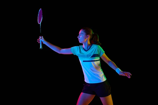 Strength and power. Dynamic movements of professional badminton player practicing with intensity against black background in neon light. Concept of sport, active and healthy lifestyle, action.