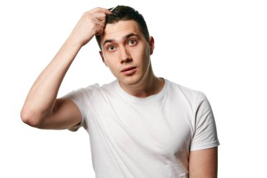 Çekici genç adamın portresi beyaz arka planda saçını tararken kameraya şaşkınlıkla bakıyor. Güzellik ve hijyen kavramı, vücut bakımı, yaşlanma karşıtı prosedürler. Boşluğu kopyala.