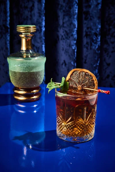 Strong alcohol cocktail with ice in glass decorated with dried citrus on toothpick served on blue bar counter. Concept of night life, party time, restaurant, celebration, holidays, New Year. Ad