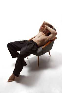 Beyaz arka planda elleri olan ve koltukta oturan genç bir adamın tam boy hava manzaralı portresi. Erkek sağlığı, güzellik, vücut ve cilt bakımı, spor anlayışı. Vücut sanatı