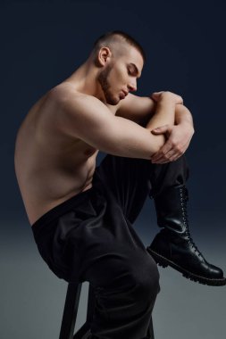 Çıplak gövdeli, sandalyede oturan ve kaslı vücudunu gösteren yakışıklı bir adamın yan görünüm portresi. Erkek sağlığı, güzellik, vücut ve cilt bakımı, spor anlayışı. Vücut sanatı